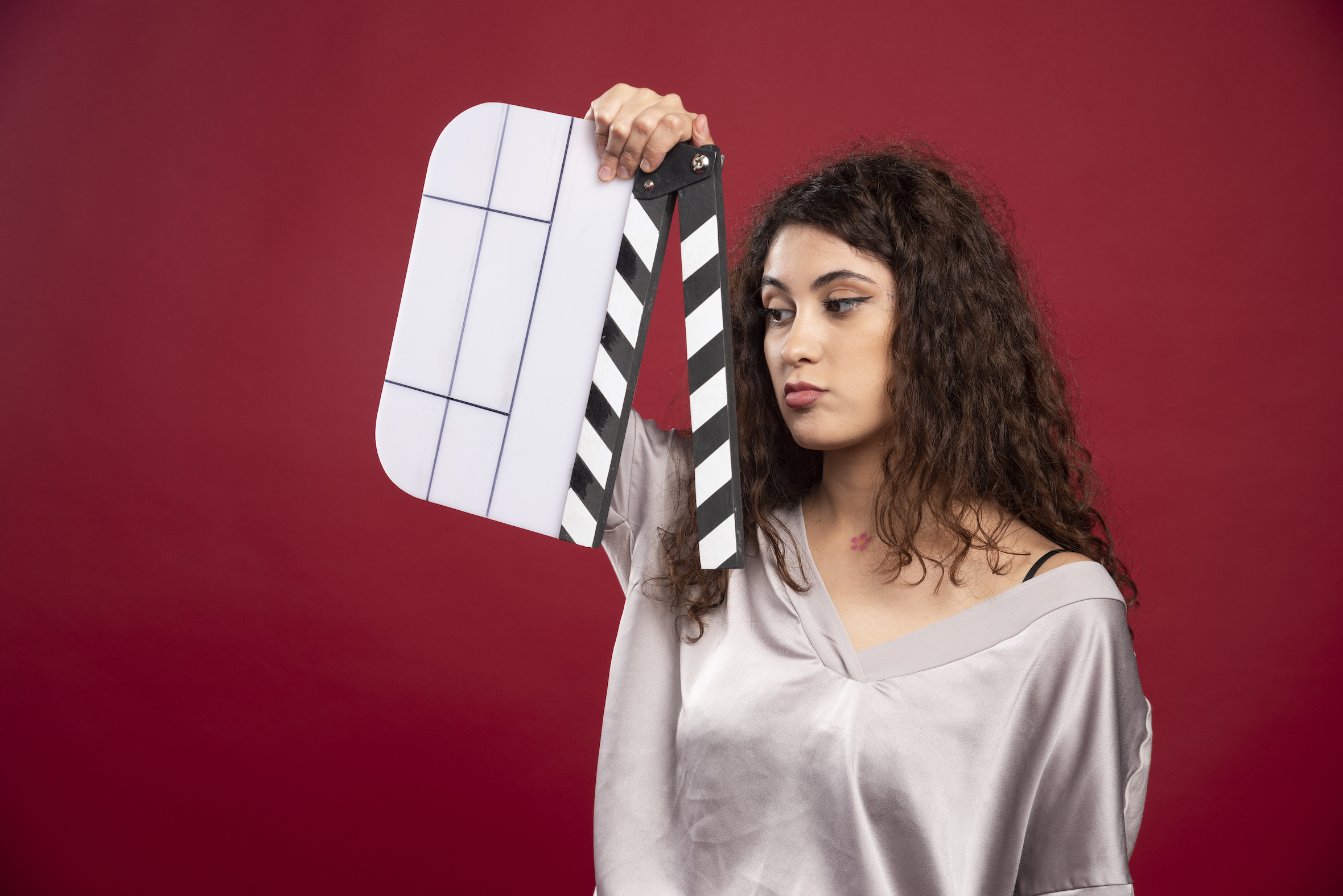 Brunette woman looking at clapperboard on red background