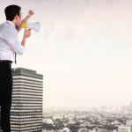 Businessman yelling through a bullhorn from the roof of a skyscraper